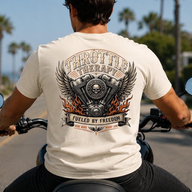 May include: A cream-colored t-shirt featuring a back graphic of a motorcycle engine with wings, a skull, and flames. The text reads THROTTLE THERAPY, FUELED BY FREEDOM, TWO WHEELS FIX EVERYTHING, and RIDE MORE WORRY LESS in a detailed, vintage-style design.