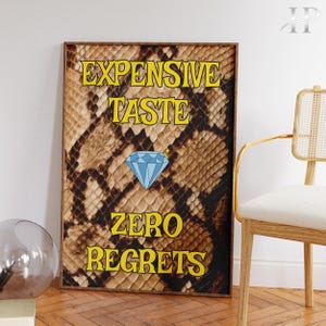 May include: A rectangular wall art print featuring a brown and black snakeskin pattern background. The text EXPENSIVE TASTE is printed in yellow at the top, followed by a blue diamond illustration, and ZERO REGRETS in yellow at the bottom.