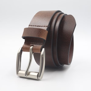 Puede incluir: Un cinturón de cuero marrón enrollado con una hebilla plateada. El cinturón está hecho de cuero liso de color marrón oscuro y tiene un diseño clásico. La hebilla es de color plateado brillante.