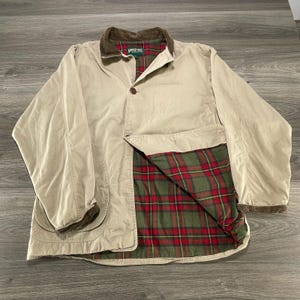 May include: A beige long-sleeve jacket with a brown corduroy collar and cuffs. The interior is lined with a green, red, and black plaid fabric. The jacket features a single button closure at the neck and a label reading American Eagle Outfitters.