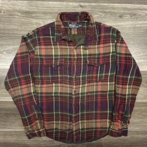 May include: A long-sleeved, button-down plaid shirt in a mix of colors including red, green, purple, and yellow. The shirt has two chest pockets and a collar. The Polo Ralph Lauren logo is visible on the label.