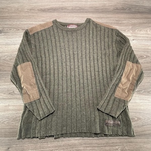 May include: An olive green ribbed long-sleeve sweater featuring tan patches on the shoulders and elbows. The garment has a crew neckline and a small rectangular patch with the text "JNCO" near the bottom hem. The sweater has a straight hemline.