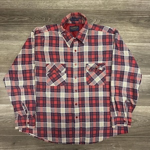 May include: A long-sleeve button-down shirt featuring a plaid pattern in shades of red, navy blue, and cream. The shirt includes a pointed collar, two chest pockets with buttoned flaps, and buttoned cuffs. The interior label reads Oakbrook.