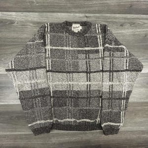 May include: A white ceramic mug with a black handle and the text "But First, Coffee" in a bold, black font. The mug is set against a blurred background, suggesting a cozy setting.