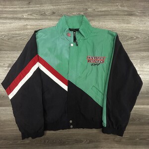 May include: A vintage racing jacket in black, green, red, and white. The jacket features the text "INTERSTATE BATTERIES Racing" on the chest. The jacket has a stand-up collar and a button-up front.