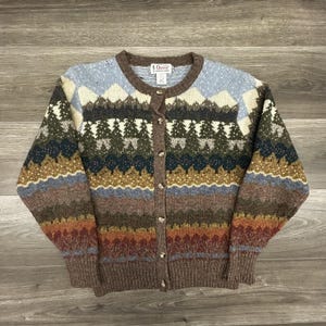 Könnte beinhalten: Braune Cardigan-Strickjacke mit Knöpfen und Landschaftsmuster. Der Pullover hat ein Muster aus Bäumen, Bergen und horizontalen Streifen in Blau-, Grün-, Braun- und Orangetönen. Der Markenname "Orvis" ist sichtbar.