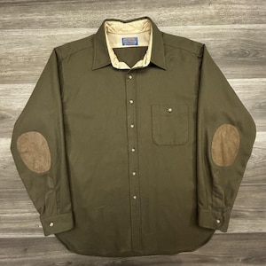 May include: An olive green long-sleeve button-down shirt featuring a cream-colored quilted inner collar lining, a single chest pocket, and brown suede-like elbow patches. The shirt has a front button placket and a Pendleton brand label.