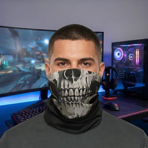 May include: A black neck gaiter featuring a detailed, high-contrast white and gray graphic print of a human skull jaw and teeth covering the lower portion of the face. The fabric is solid black, providing a stark background for the skull design.