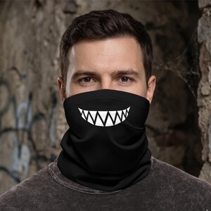 May include: A black neck gaiter featuring a white graphic print of a wide, toothy grin. The fabric is solid black and covers the lower portion of the face, extending from the bridge of the nose down to the neck, with a sharp, stylized design.