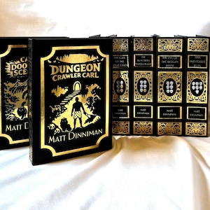 May include: A set of black books with gold lettering and illustrations. Titles include "Dungeon Crawler Carl" and "The Butcher's Masquerade." The author's name, Matt Dinniman, is displayed. The books have gold detailing and decorative edges.