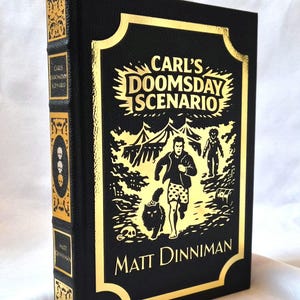 Puede incluir: Un libro de tapa dura negro titulado Carl's Doomsday Scenario de Matt Dinniman. La portada presenta un estampado de l&aacute;mina dorada con una ilustraci&oacute;n central de una persona corriendo con un gato, rodeada de tiendas de campa&ntilde;a y una calavera.