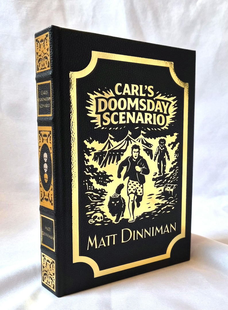 Puede incluir: Un libro de tapa dura negro titulado Carl's Doomsday Scenario de Matt Dinniman. La portada presenta un estampado de l&aacute;mina dorada con una ilustraci&oacute;n central de una persona corriendo con un gato, rodeada de tiendas de campa&ntilde;a y una calavera.
