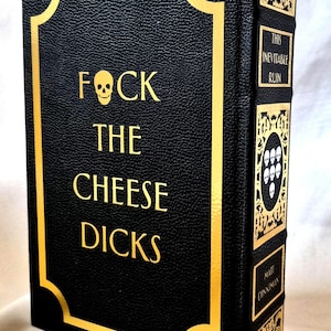 Puede incluir: Un libro de tapa dura negro con letras doradas y un icono de calavera. La portada dice FOCK THE CHEESE DICKS. El lomo presenta paneles decorativos dorados, un emblema de calavera y el texto THIS INEVITABLE RUIN y MATT DINNIMAN.