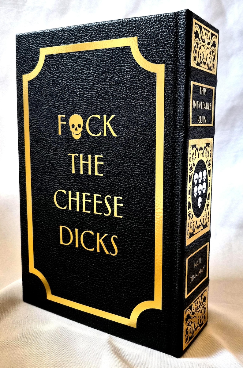 Puede incluir: Un libro de tapa dura negro con letras doradas y un icono de calavera. La portada dice FOCK THE CHEESE DICKS. El lomo presenta paneles decorativos dorados, un emblema de calavera y el texto THIS INEVITABLE RUIN y MATT DINNIMAN.
