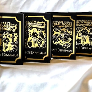 Puede incluir: Un conjunto de siete libros de tapa dura titulados Dungeon Crawler Carl de Matt Dinniman. Cada libro negro presenta ilustraciones y texto en l&aacute;mina dorada en la portada, representando varios personajes y escenas de la serie.