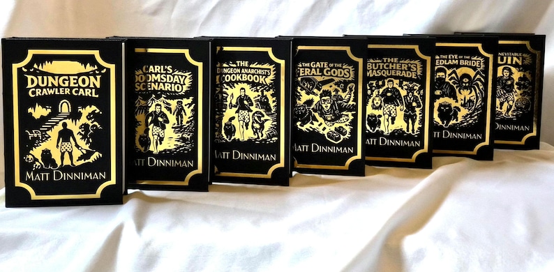 Puede incluir: Un conjunto de siete libros de tapa dura titulados Dungeon Crawler Carl de Matt Dinniman. Cada libro negro presenta ilustraciones y texto en l&aacute;mina dorada en la portada, representando varios personajes y escenas de la serie.