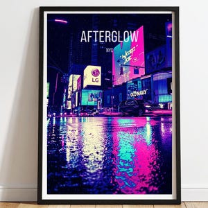 Puede incluir: Impresión artística enmarcada de un paisaje urbano iluminado con neones por la noche, con el texto "AFTERGLOW NYC" en la parte superior. La imagen presenta vibrantes tonos rosas, azules y morados que se reflejan en una calle mojada, con vallas publicitarias iluminadas y un coche.