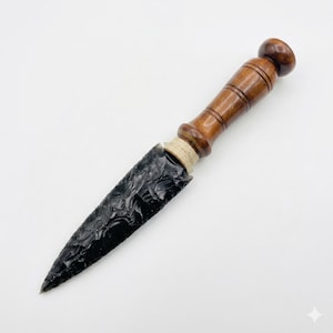 May include: An obsidian knife with a dark, textured blade and a wooden handle. The handle is a rich brown colour with a rounded end. The blade is a deep black, with a sharp point.