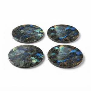 Op de afbeelding: Een set van vier ronde onderzetters gemaakt van gepolijste labradorietsteen. Elke onderzetter heeft een donker, veelzijdig oppervlak met iriserende blauwe, groene en gouden minerale insluitingen die een reflecterend mozaïekpatroon vormen.