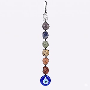Op de afbeelding: Een hangende chakra kristallen zonnevanger met zeven gekleurde stenen in een net, een zwart koord en een blauwe evil eye bedel. De stenen zijn wit, paars, blauw, groen, beige, oranje en rood.