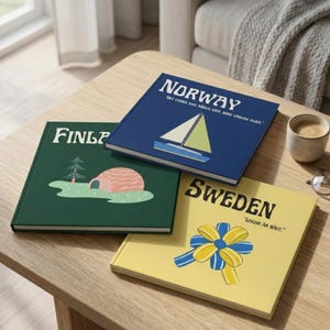 May include: Three hardcover books with country names on the covers: "NORWAY" in navy blue with a sailboat graphic, "FINLP" in green with a cartoon landscape, and "SWEDEN" in yellow with a bow graphic. The books are on a wooden table.