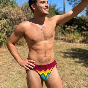 Puede incluir: Una braga de bikini de ganchillo color granate con un vibrante patrón de chevrón en amarillo, naranja, verde y azul en la parte delantera. La prenda incluye lazos laterales para un ajuste regulable, confeccionada con hilo texturizado.