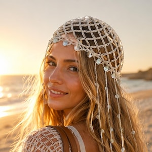 May include: A cream-colored crochet headpiece featuring a net-like pattern adorned with small, circular, reflective silver-toned discs. The headpiece includes long, dangling strands of crochet thread that are also embellished with these metallic discs.