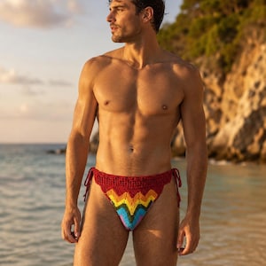 Puede incluir: Una braga de bikini de ganchillo con cintura y lazos laterales en rojo oscuro, con un patrón de chevrón en amarillo, naranja, verde, azul y morado en la parte delantera. La prenda está confeccionada en hilo con un patrón de punto texturizado.
