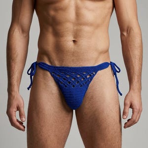 Puede incluir: Una braguita de bikini de ganchillo en color azul real vibrante que presenta una bolsa de punto sólido, un patrón de diamantes calado en la sección superior y finas tiras laterales trenzadas anudadas en cada cadera para ajustar la prenda.