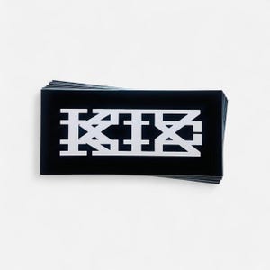 May include: A stack of black rectangular cards with a white geometric design. The design features the letters "KIX" in a stylized, blocky font. The cards are stacked neatly against a white background.