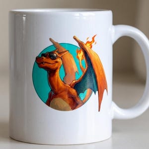 Può includere: Una tazza in ceramica bianca con un'illustrazione grafica di una creatura arancione simile a un drago che indossa occhiali da sole neri. La creatura è posizionata su uno sfondo circolare color ottanio, con fiamme arancioni e gialle.