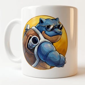 Op de afbeelding: Een witte keramische mok met een grafische illustratie van een blauw, schildpadachtig wezen dat een zwarte zonnebril draagt. Het wezen heeft een bruin schild met twee metalen kanonnen op de rug, tegen een gele cirkelvormige achtergrond.