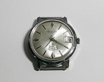 Puede incluir: Un reloj de pulsera Beacon Hill Incabloc plateado con esfera plateada. El reloj tiene visualización de fecha, indicador de día de la semana y correa de acero inoxidable. La esfera del reloj tiene un diámetro de aproximadamente 3,8 cm.
