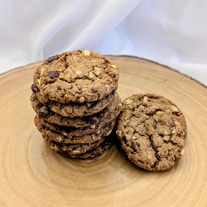 May include: A stack of six round oatmeal chocolate chip cookies next to a single cookie. The cookies are brown with visible rolled oats and dark chocolate chips throughout the textured surface, showcasing a rustic, baked appearance.