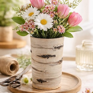 May include: A birch bark vase with pink tulips, white daisies, and small pink flowers. The vase is on a wooden tray, with scissors and twine. The text "Rustic Birch Bark Vase" is at the top of the image.
