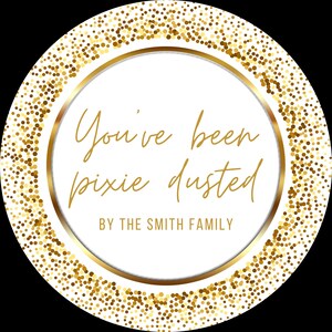May include: A circular graphic with a white background, gold text, and glitter accents. The text says "You've been pixie dusted" and "BY THE SMITH FAMILY". The outer edge has a gold glitter border.