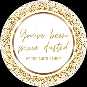 May include: A circular graphic with a white background, gold text, and gold glitter accents. The text says "You've been pixie dusted" and "BY THE SMITH FAMILY". The outer edge is decorated with gold glitter.