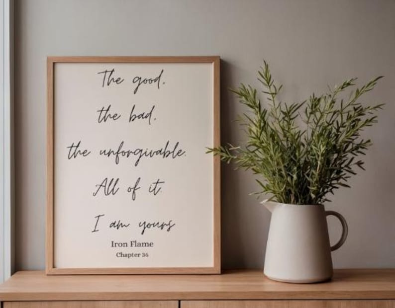 Puede incluir: Un cuadro enmarcado con el texto "The good, the bad, the unforgivable. All of it, I am yours." Una jarra blanca con asa contiene ramas verdes. El marco es de color marr&oacute;n claro y el fondo es neutro.