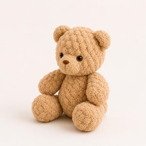 May include: A tan-colored teddy bear with a textured, knitted appearance. The bear has small, round ears, a brown nose, and dark eyes. It is sitting with its arms and legs in a relaxed position, a classic children's toy.