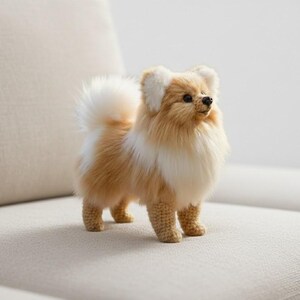 May include: A handmade, plush Pomeranian dog figurine. The dog has a fluffy, two-tone coat of light brown and white, with a matching tail and ears. The dog is standing on a neutral-colored surface, with a crocheted body and legs.