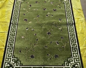 May include: A rectangular area rug featuring a vibrant green field decorated with scattered dark floral motifs on thin winding vines. The rug is framed by a wide border with a white Greek key pattern on a dark brown background and fringe.