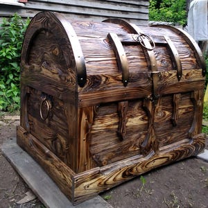 Puede incluir: Un gran cofre de madera hecho a mano con tapa abovedada. El cofre presenta bandas met&aacute;licas y un pestillo, con un acabado marr&oacute;n oscuro y veta de madera visible. El dise&ntilde;o sugiere un estilo vintage o antiguo, adecuado para almacenamiento o decoraci&oacute;n.