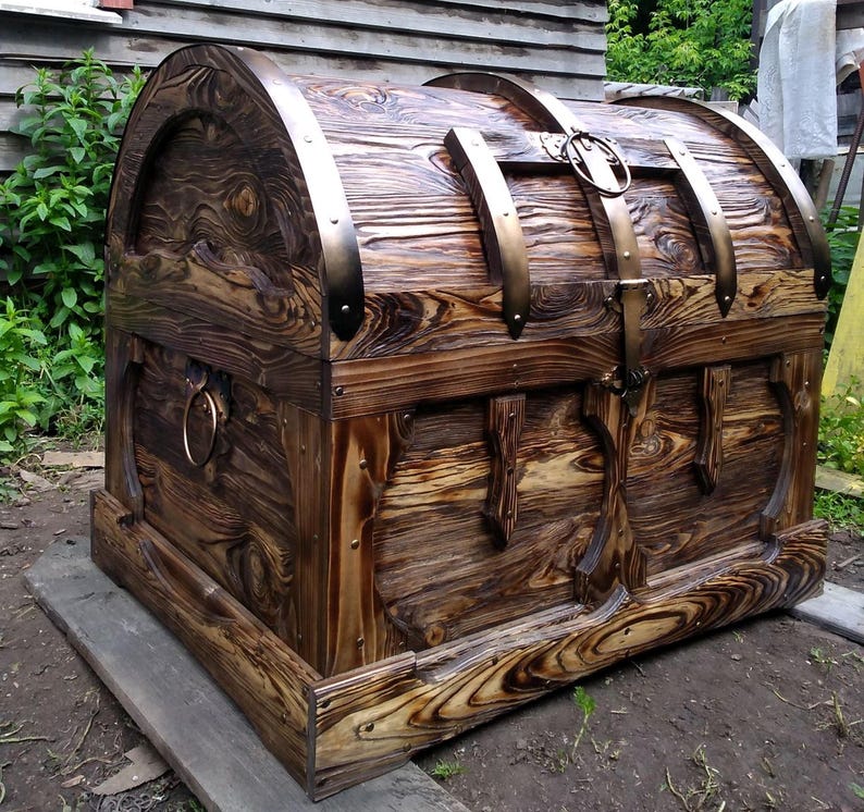 Puede incluir: Un gran cofre de madera hecho a mano con tapa abovedada. El cofre presenta bandas met&aacute;licas y un pestillo, con un acabado marr&oacute;n oscuro y veta de madera visible. El dise&ntilde;o sugiere un estilo vintage o antiguo, adecuado para almacenamiento o decoraci&oacute;n.