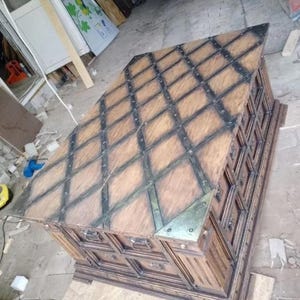 May include: A large, wooden chest with a diamond pattern on the top and metal accents. The chest is brown with black metal straps and corner pieces. It has multiple drawers and a decorative base.