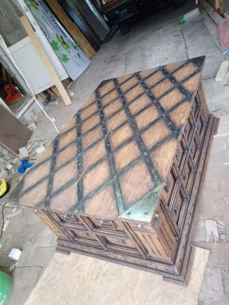 May include: A large, wooden chest with a diamond pattern on the top and metal accents. The chest is brown with black metal straps and corner pieces. It has multiple drawers and a decorative base.