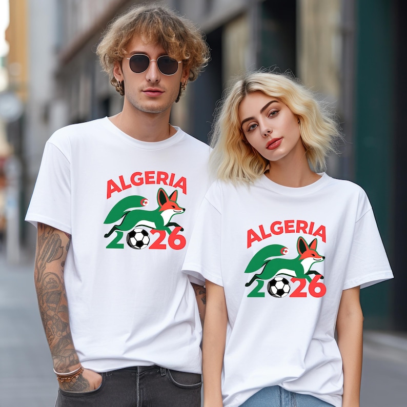 May include: White t-shirts with a graphic design featuring the word "ALGERIA" in red, a green and white fox, a soccer ball, and the number "2026" in red and green. The shirts are worn by two people.