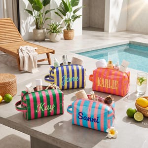 Puede incluir: Cuatro neceseres rectangulares con rayas verticales en varias combinaciones de colores. Cada bolsa presenta un nombre personalizado en letra cursiva o de imprenta: Jane, Karlie, Kay y Sanni. Las bolsas están llenas de frascos de cuidado personal.