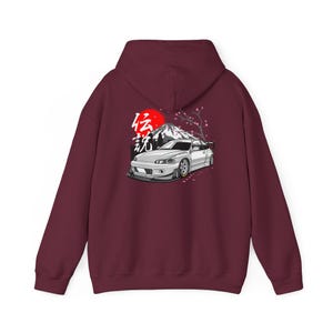 Könnte beinhalten: Burgunderfarbener Kapuzenpullover mit einer Grafik eines weißen Autos, eines Berges, einer roten Sonne und japanischem Text. Das Design beinhaltet Kirschblüten. Der Hoodie hat eine Kapuze und eine Kängurutasche.