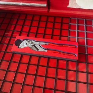 Op de afbeelding: Een Knipex tang met rode handgrepen en een zilveren kop, rustend in een rode schuimrubberen inzet. Het gereedschap wordt getoond in een rode gereedschapskistlade.