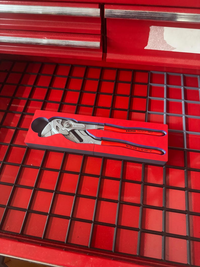Op de afbeelding: Een Knipex tang met rode handgrepen en een zilveren kop, rustend in een rode schuimrubberen inzet. Het gereedschap wordt getoond in een rode gereedschapskistlade.